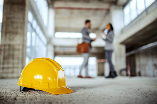 A hard hat on the floor with two people discussing in the background at a real estate construction site.