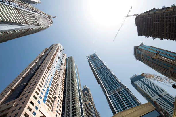 A low-angle view of towering commercial buildings and construction cranes under a clear sky.